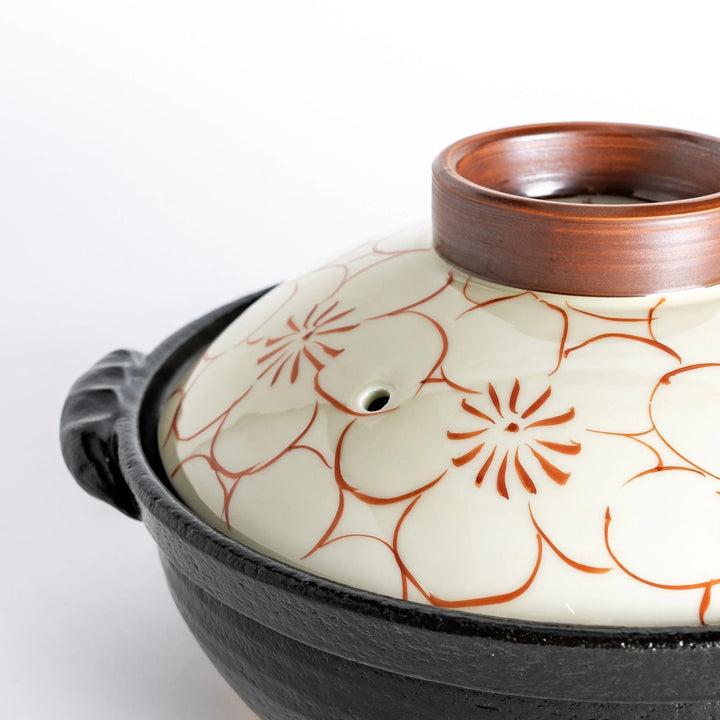 A 8-inch donabe with a vibrant red blossom pattern lid and black pot.