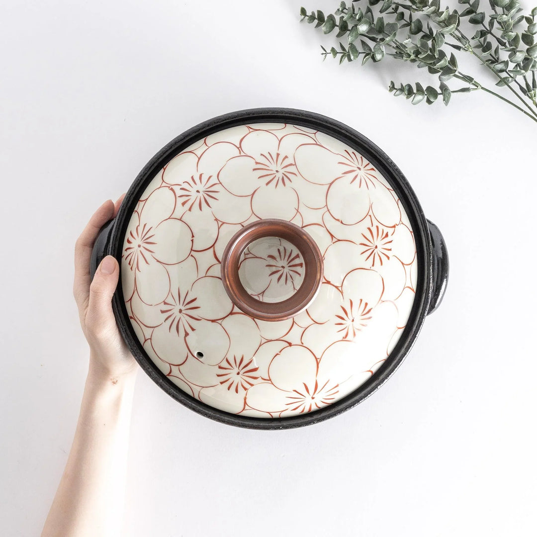 A donabe with a vibrant red floral pattern on white lid and black pot.