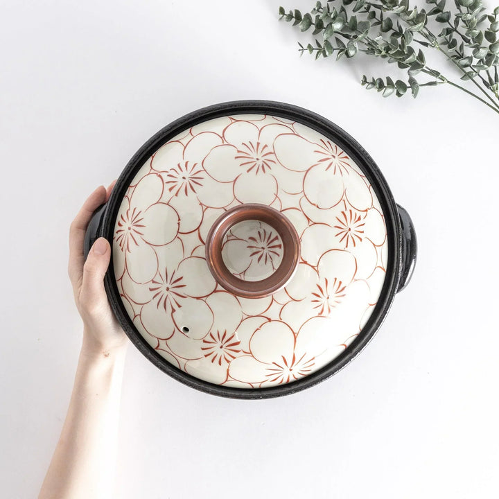 A donabe with a vibrant red floral pattern on white lid and black pot.