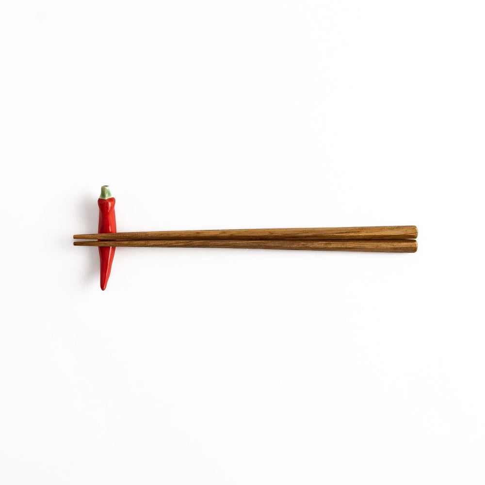 Wooden chopsticks resting on a red chili pepper-shaped chopstick rest, combining practical use and playful design.
