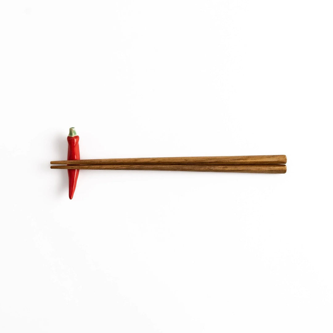 Wooden chopsticks resting on a red chili pepper-shaped chopstick rest, combining practical use and playful design.