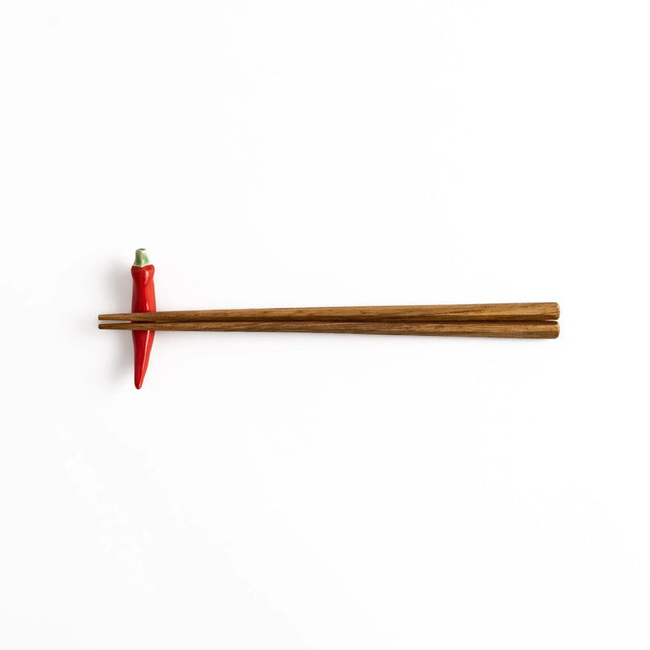 Wooden chopsticks resting on a red chili pepper-shaped chopstick rest, combining practical use and playful design.