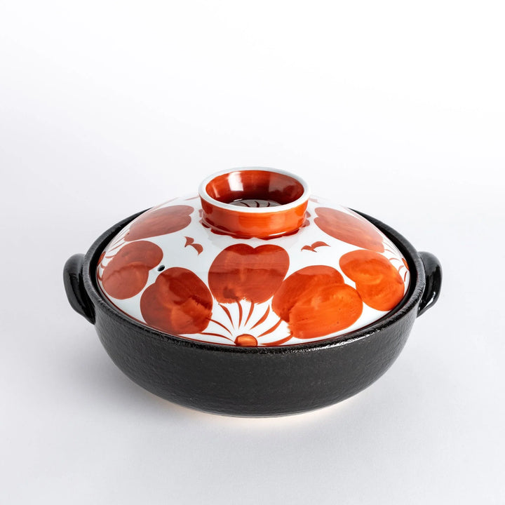 A beautifully crafted donabe with a vibrant red floral pattern on the lid, perfect for serving various hot dishes.