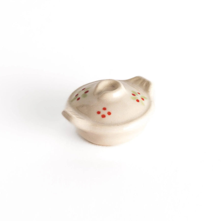Earthen pot chopstick rest with red flower and green leaf on beige glaze showcasing rustic Japanese charm.