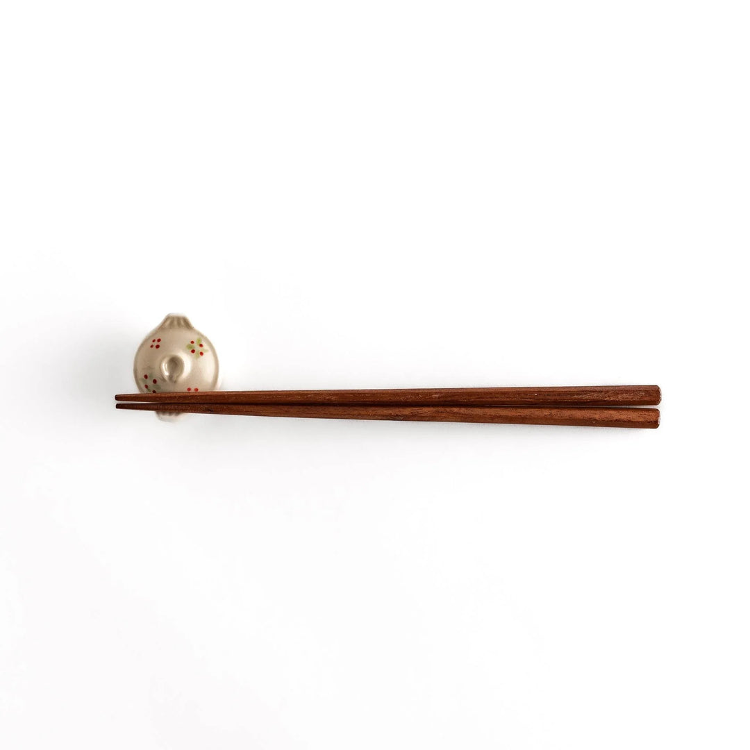 Earthen pot chopstick rest with red flower and green leaf on beige glaze showcasing rustic Japanese charm.