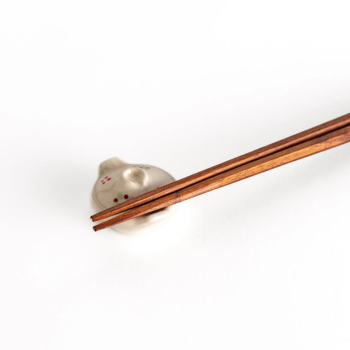 Earthen pot chopstick rest with red flower and green leaf on beige glaze showcasing rustic Japanese charm.