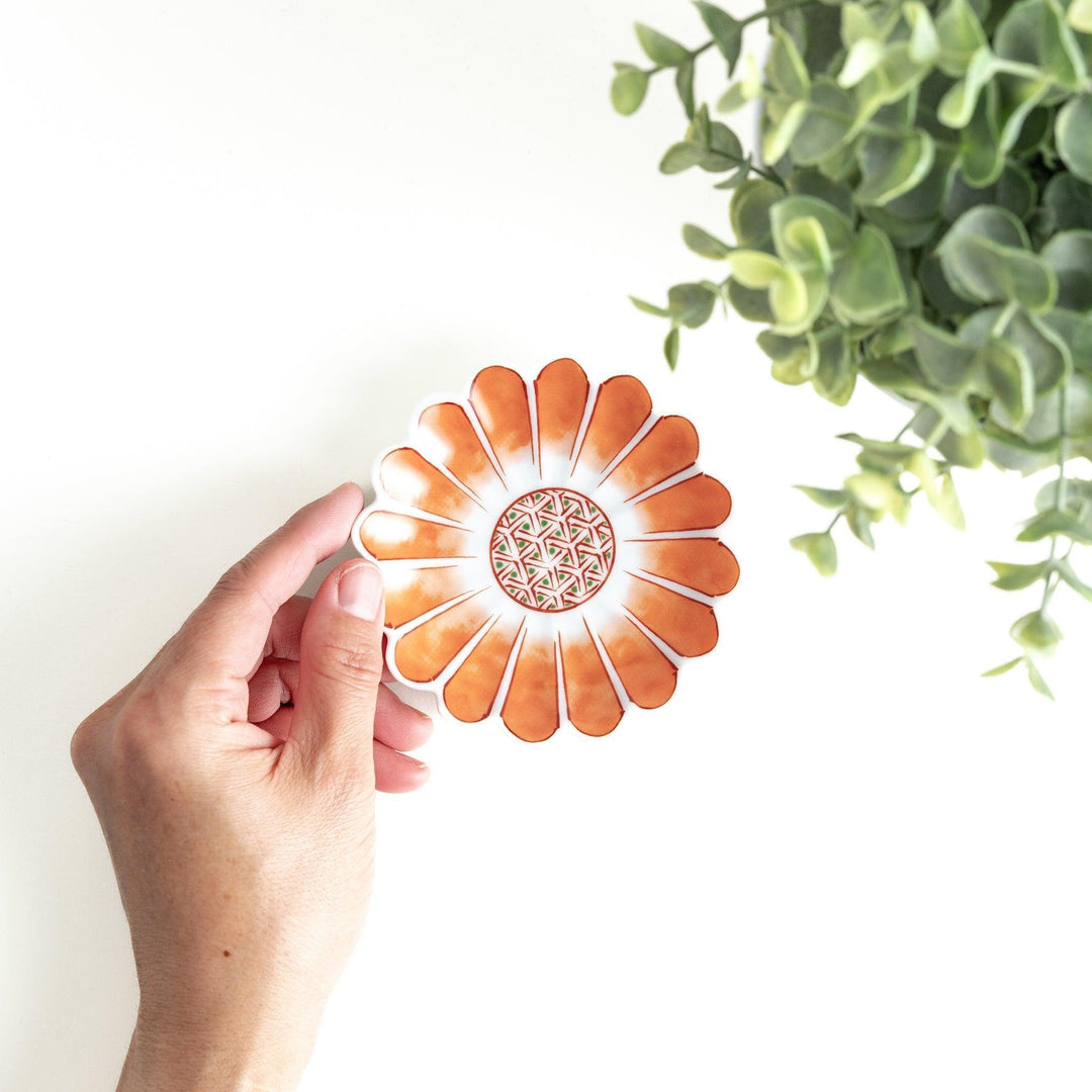 A small, scalloped-edge porcelain dish with orange chrysanthemum petal designs and a geometric center.