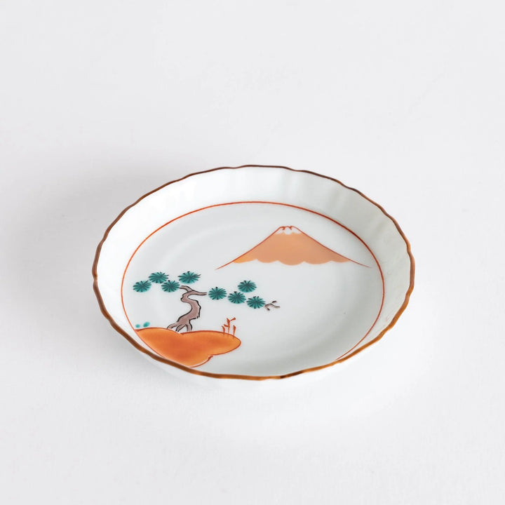 Round Japanese ceramic dish with Mount Fuji and red pine grove design scalloped edge and orange rim.
