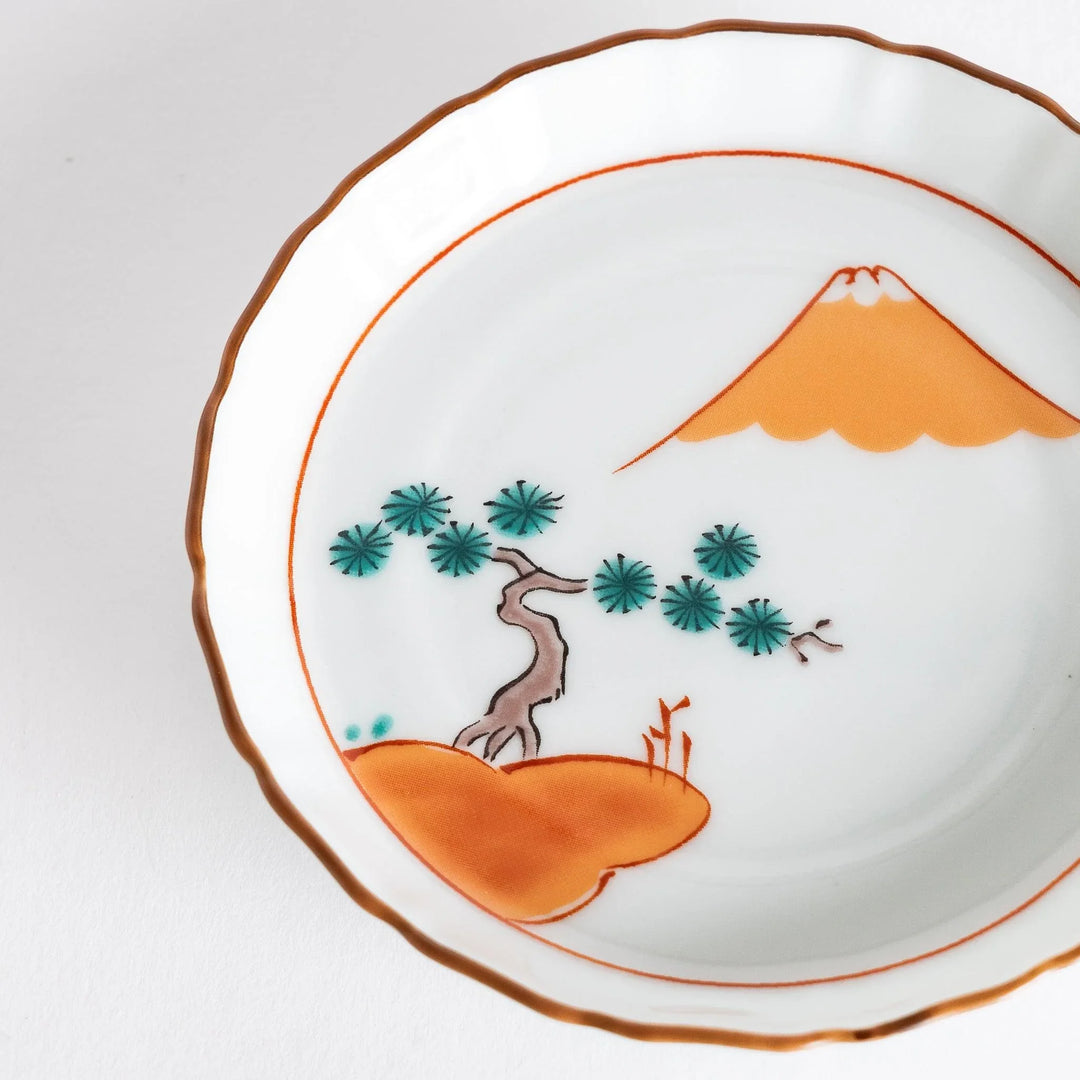 Round Japanese ceramic dish with Mount Fuji and red pine grove design scalloped edge and orange rim.