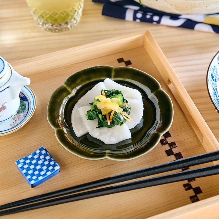 An olive-colored, flower-shaped plate holding a small serving of Japanese pickled vegetables, placed on a wooden tray.