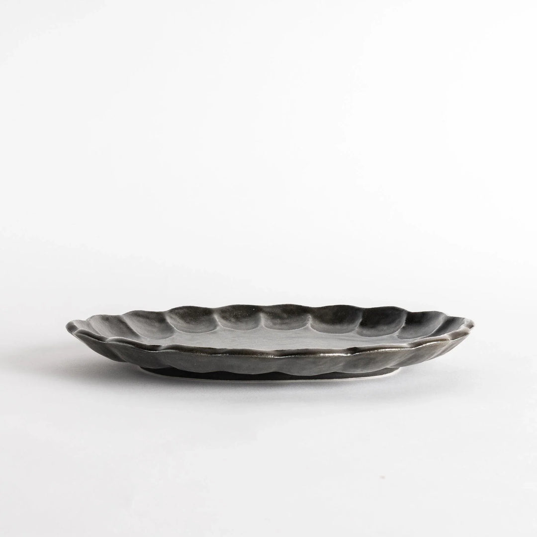 A white ceramic serving plate with a delicate, scalloped oval shape. Available in black or white.