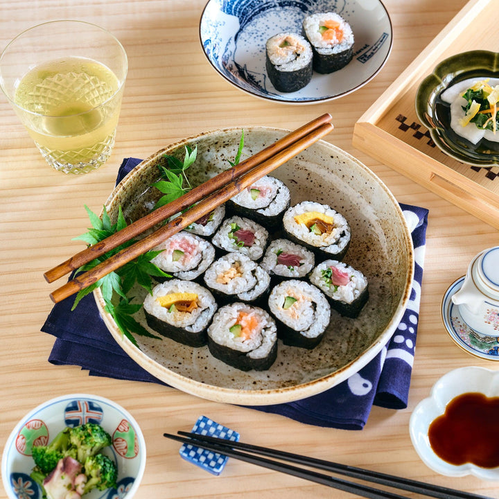 A rustic beige plate with a slightly deep shape, filled with colorful sushi rolls, beautifully presented on a dining table.