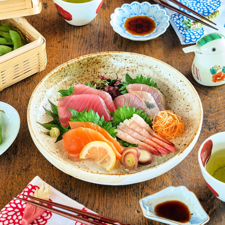 Earth-tone pasta bowl with speckled glaze and freeform shape, showcasing colorful sashimi and garnishes on a wooden surface.