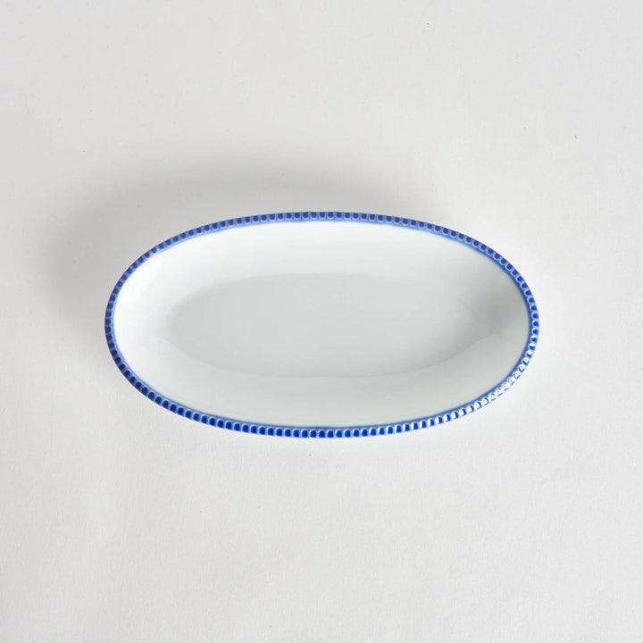 Top-down view of an oval salad platewith rustic scalloped edges and a blue beaded rim, showcasing its simple, elegant design.