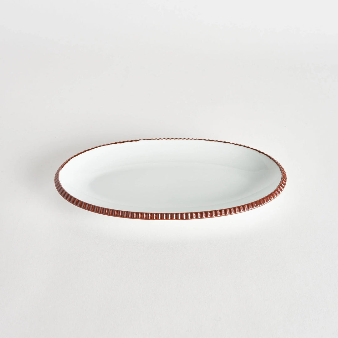 Angled view of an oval salad plate with a brown-colored scalloped edge.