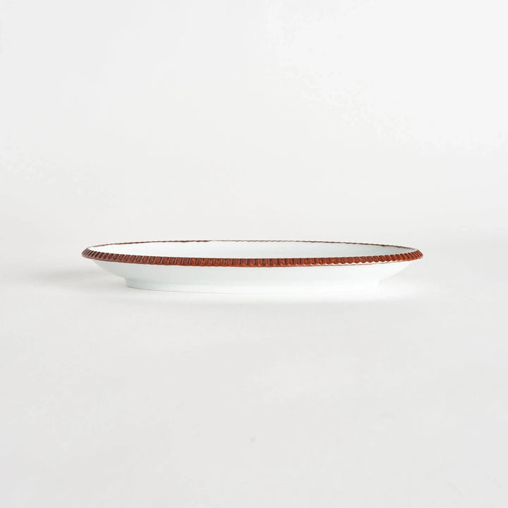 Side view of an oval salad plate featuring a warm brown-colored scalloped edge.
