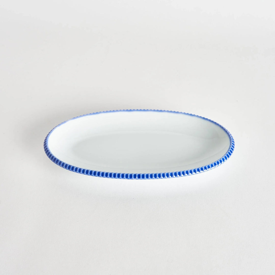 Angled view of an oval salad plate featuring a scalloped blue edge.