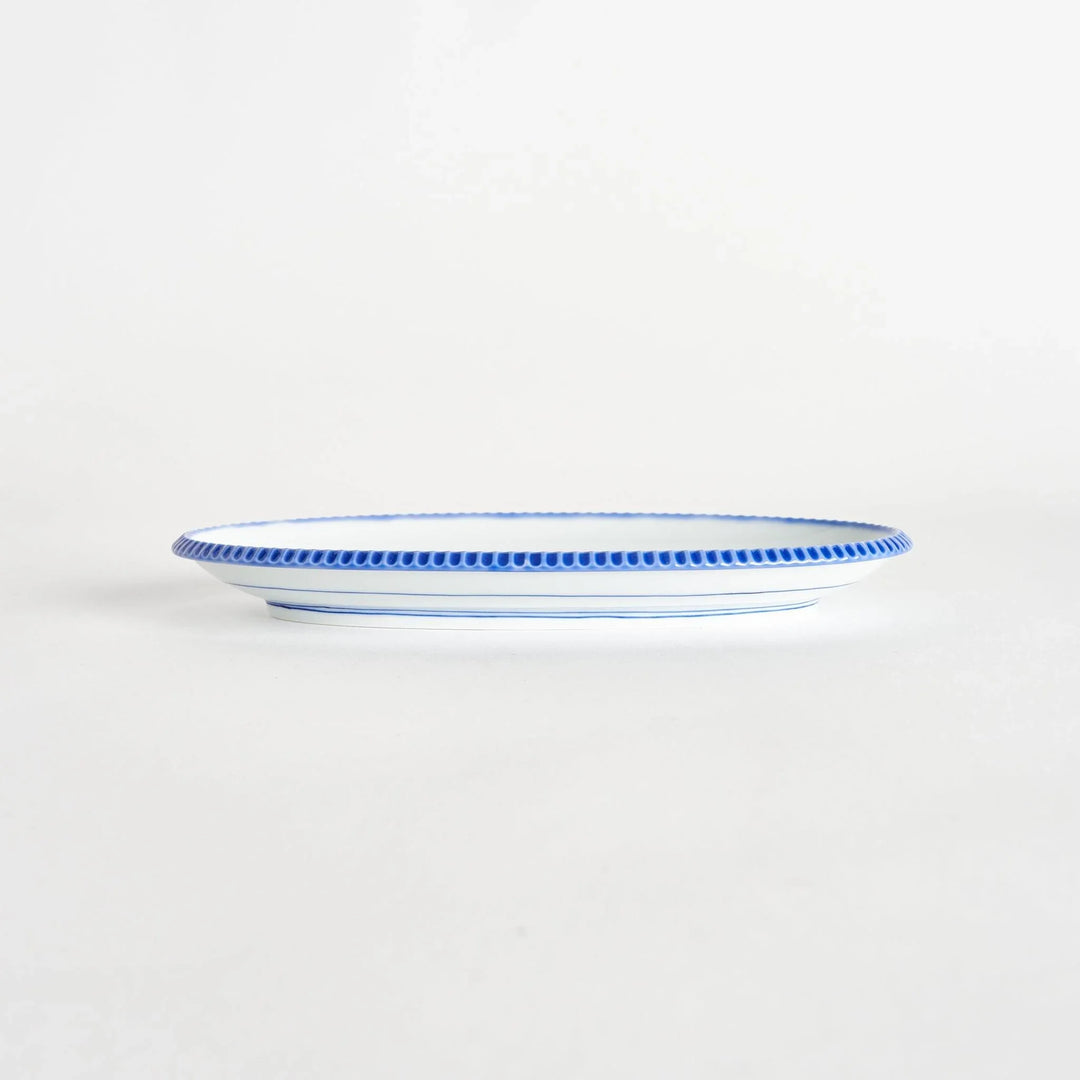 Side view of an oval salad plate showcasing its delicate shape and scalloped blue edge.
