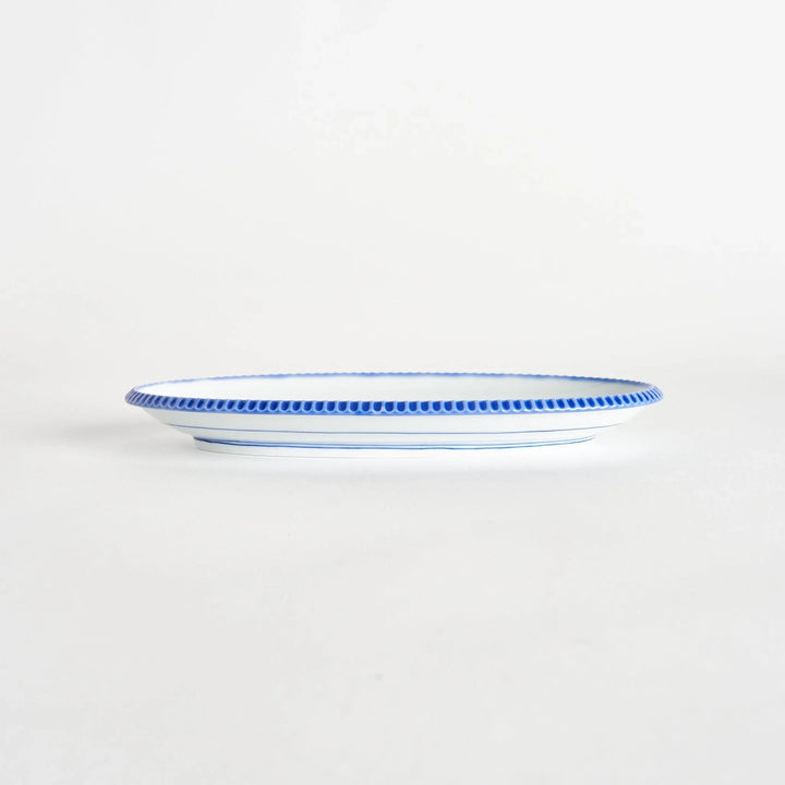 Side view of an oval salad plate showcasing its delicate shape and scalloped blue edge.