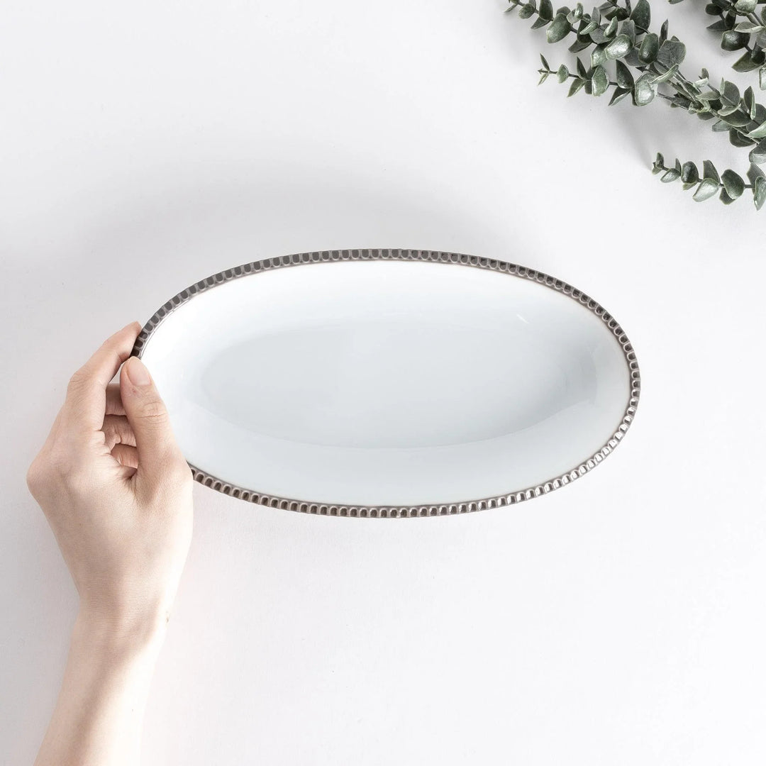 Handheld top-down view of an oval salad plate with an olive-colored scalloped edge.