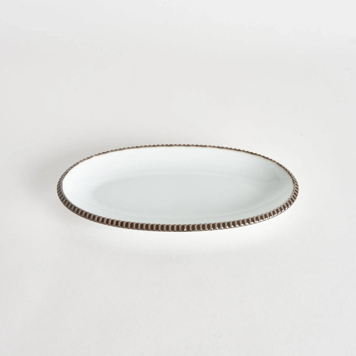 Angled view of an oval salad plate with an olive-colored scalloped edge.