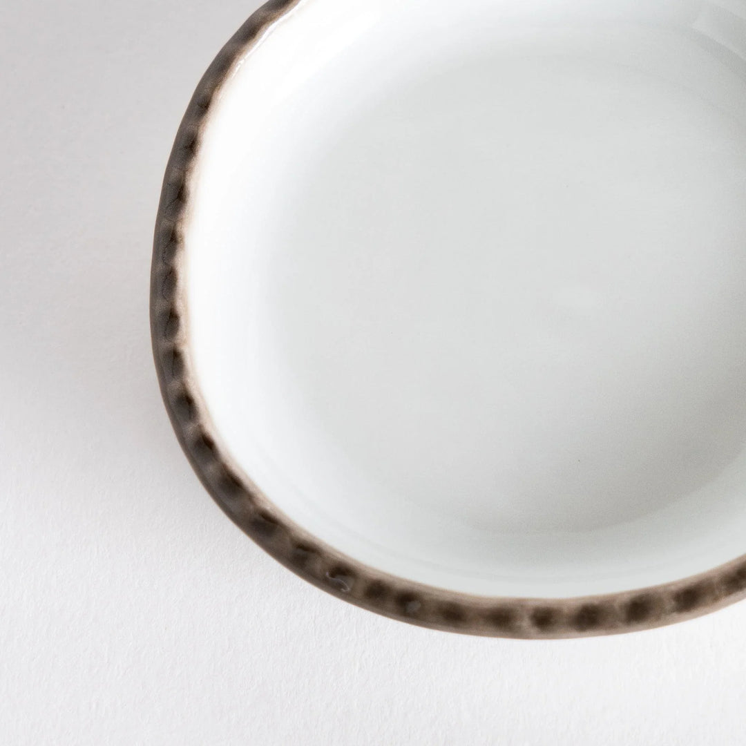 Profile view of a small oval sauce dish featuring a scalloped edge and a brown dotted rim.