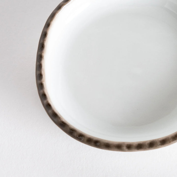 Profile view of a small oval sauce dish featuring a scalloped edge and a brown dotted rim.