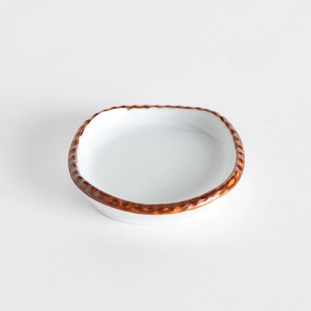 Hand holding a small oval sauce dish, showcasing its smooth white interior and the scalloped olive-colored edge.