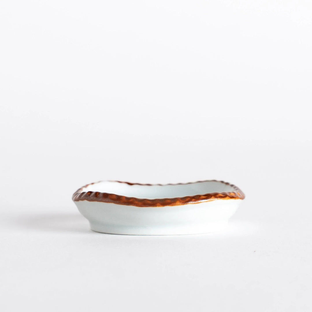 Side view of a small oval sauce dish highlighting the smooth interior and the olive-colored scalloped edge.