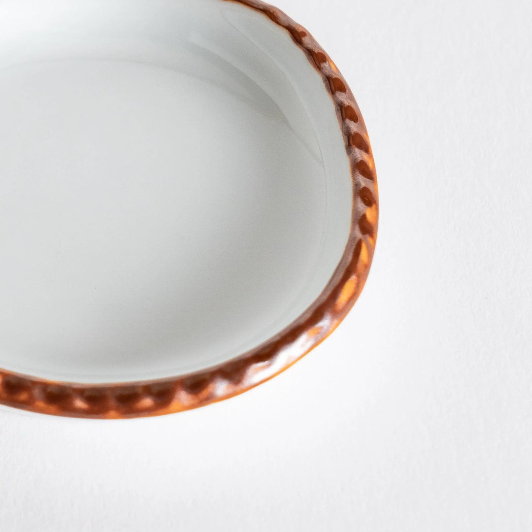 Profile view of a small oval sauce dish emphasizing the elegant olive-colored edge.