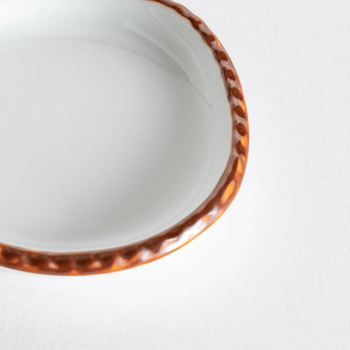 Profile view of a small oval sauce dish emphasizing the elegant olive-colored edge.