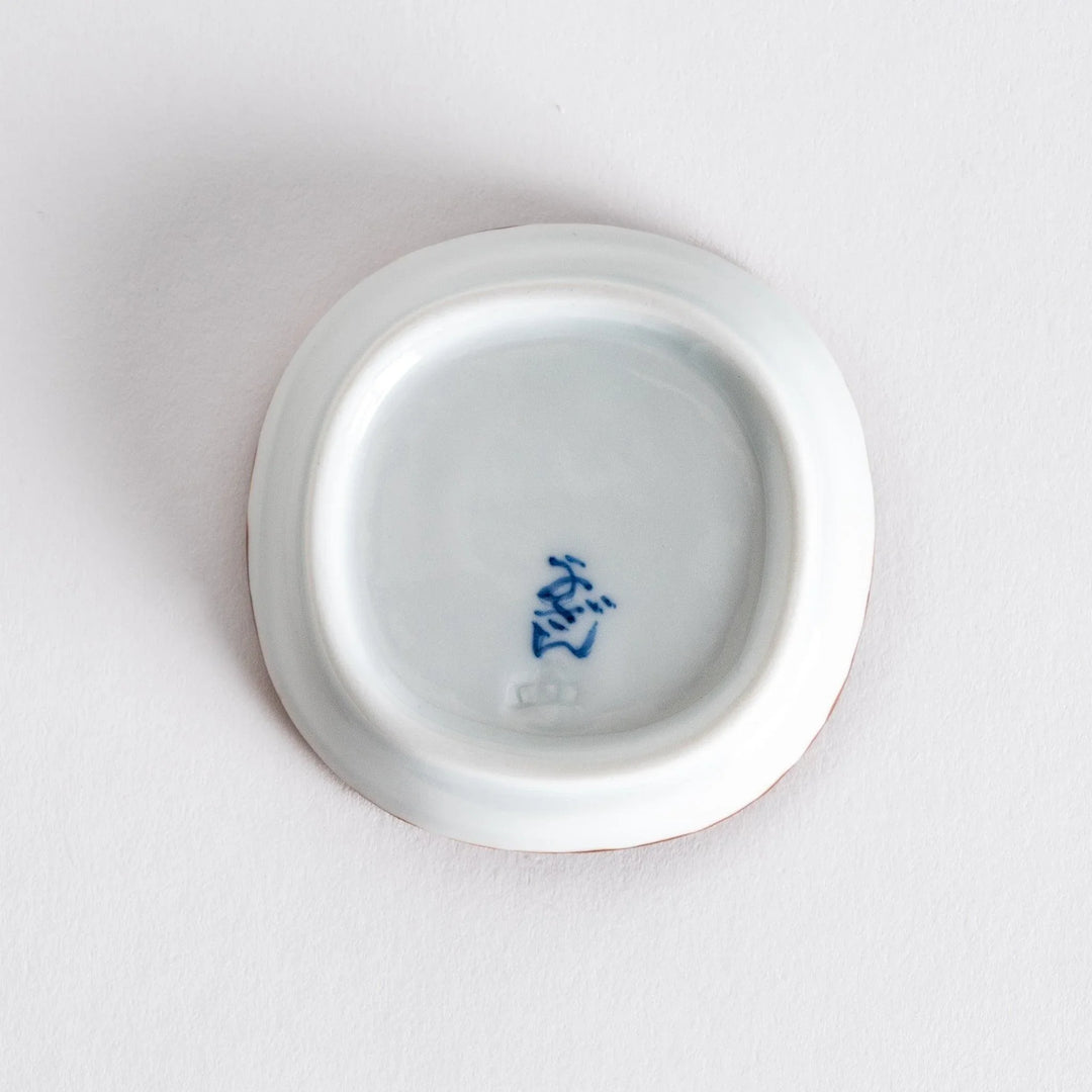 Close-up of the interior of a small oval sauce dish, showing its smooth white surface and the olive-colored scalloped edge.