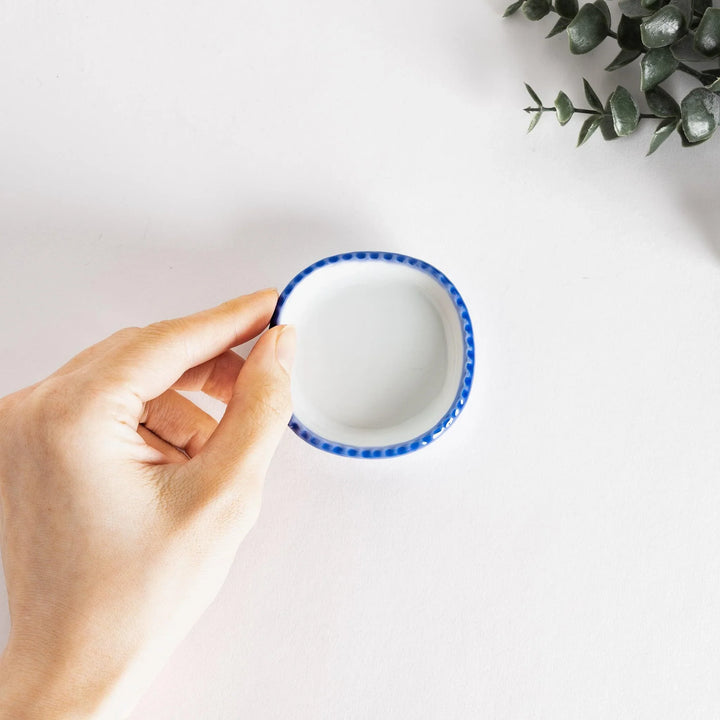 Hand holding a small, square condiment dish with blue detailing, showcasing its delicate design.