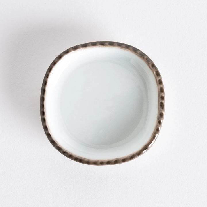 Top view of a small oval sauce dish featuring a scalloped edge and a brown dotted rim.