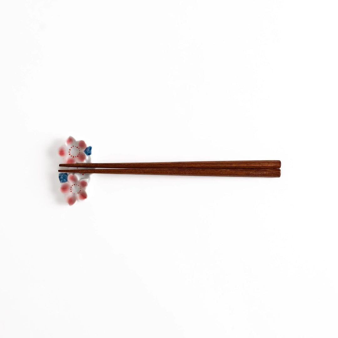 Sakura Blossom Chopstick Rest holding wooden chopsticks, showcasing its intricate floral design and functional charm.
