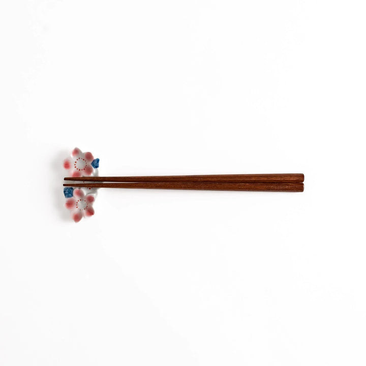 Sakura Blossom Chopstick Rest holding wooden chopsticks, showcasing its intricate floral design and functional charm.