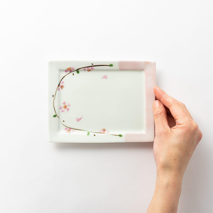 Dessert plate held in hand, viewed from above, featuring a cherry blossom design on one corner.