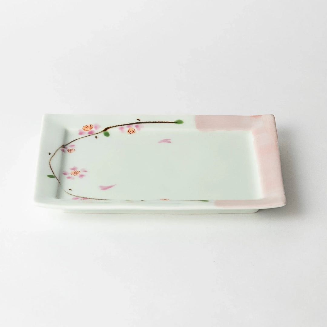 Dessert plate viewed at an angle, showing the pink cherry blossoms and delicate green accents along the edges.
