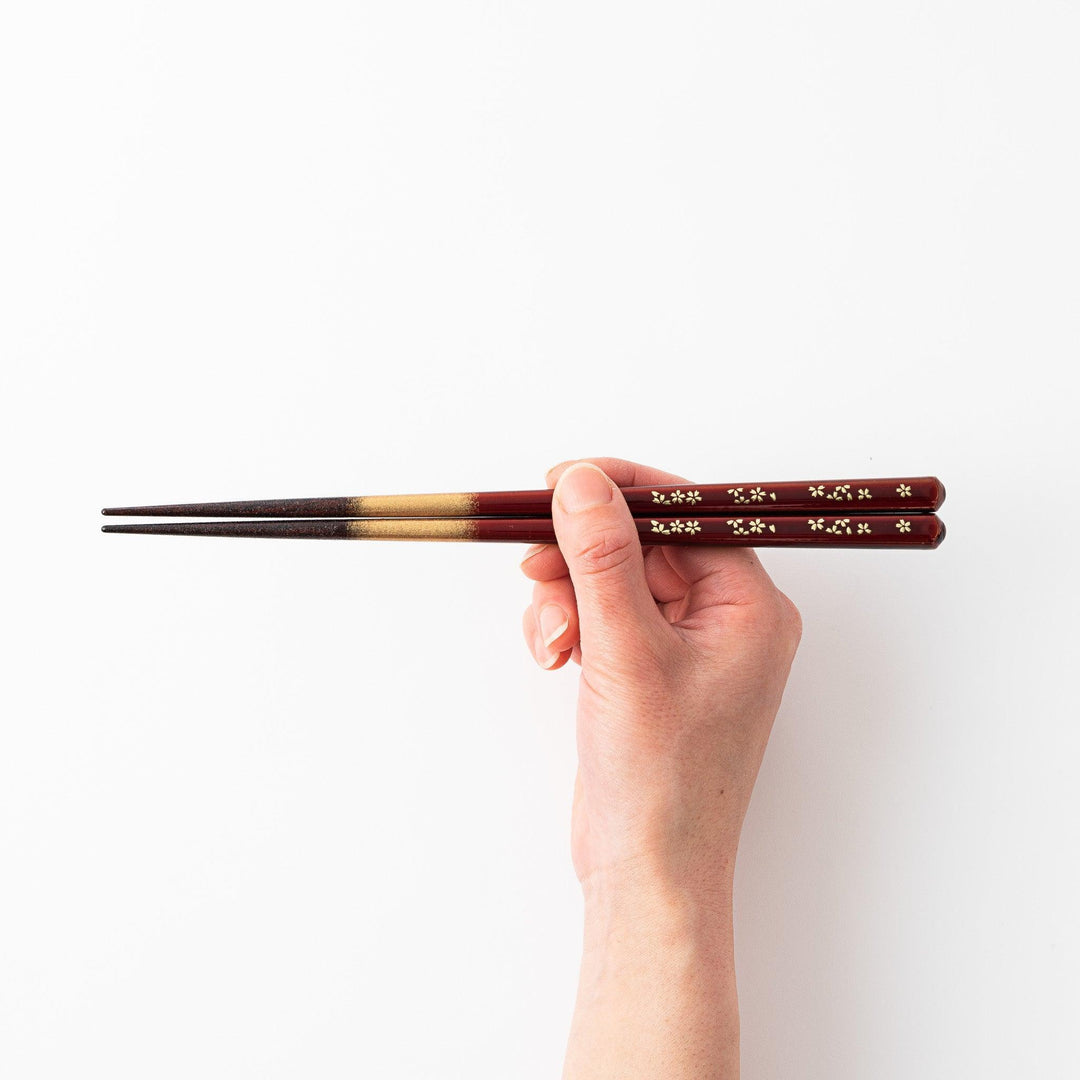 Elegant red and brown lacquered chopsticks adorned with delicate gold cherry blossom motifs, featuring a gradient of gold for added sophistication.