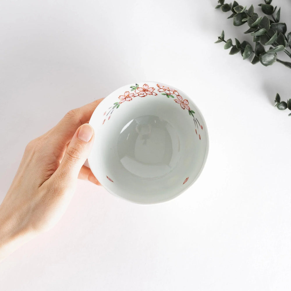A white rice bowl adorned with delicate pink sakura blossoms and green leaves.