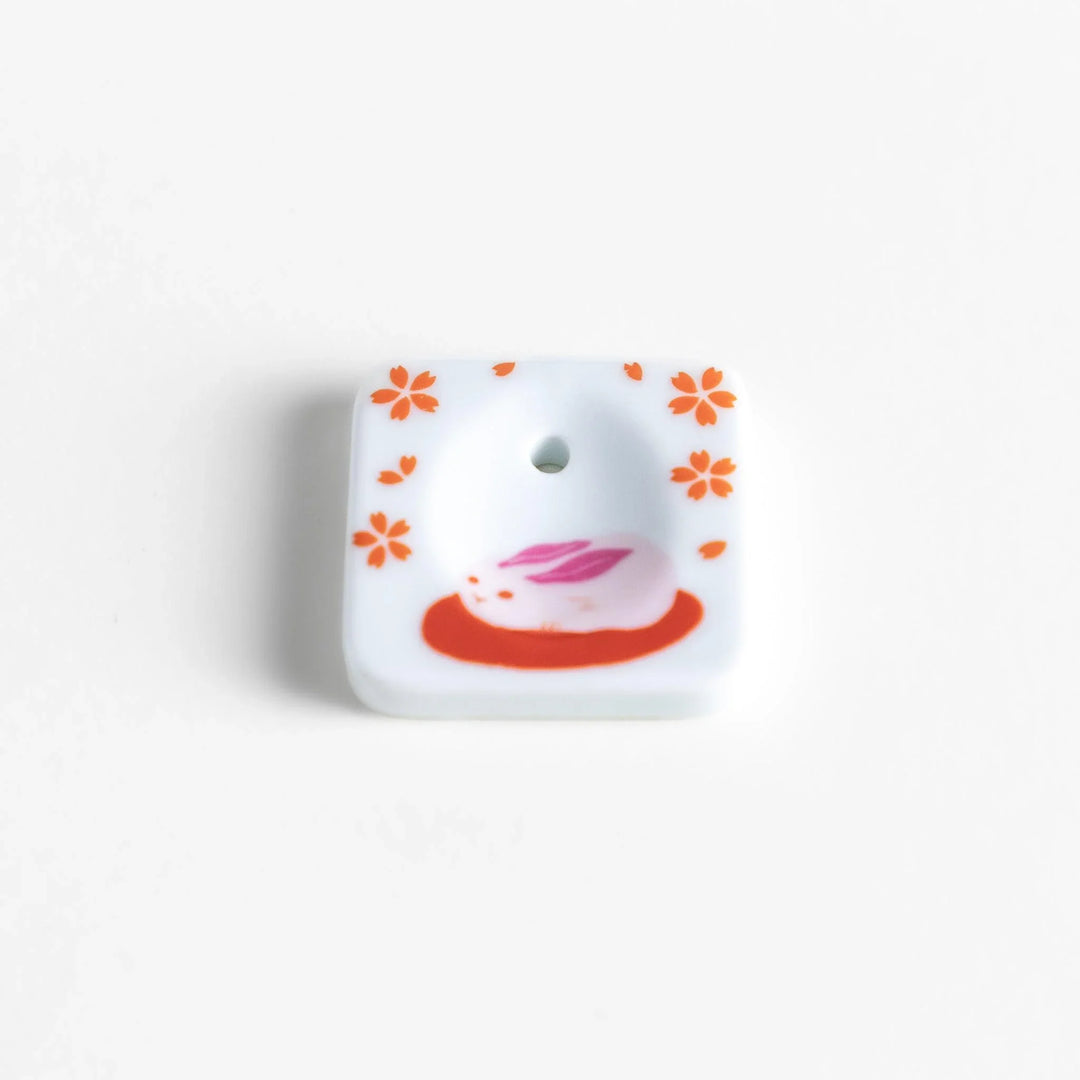 Square ceramic incense holder with sakura rabbit design in pink and red crafted to hold incense with elegance.