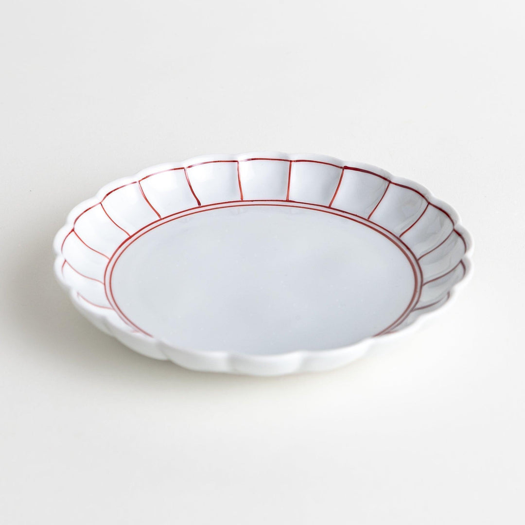 White dessert plate with scalloped edges, outlined in a thin blue or red line.