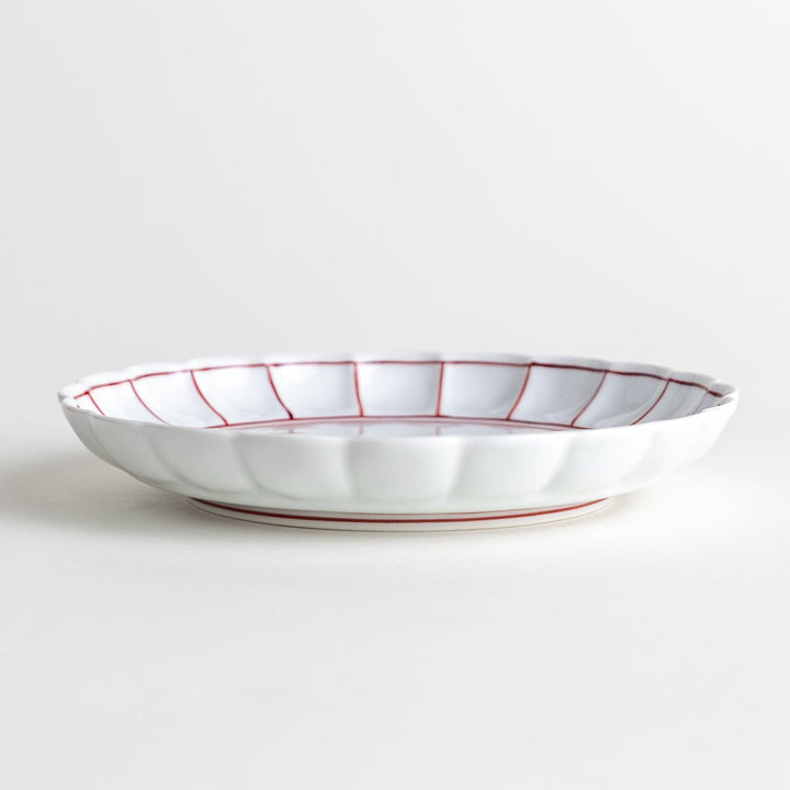 White dessert plate with scalloped edges, outlined in a thin blue or red line.