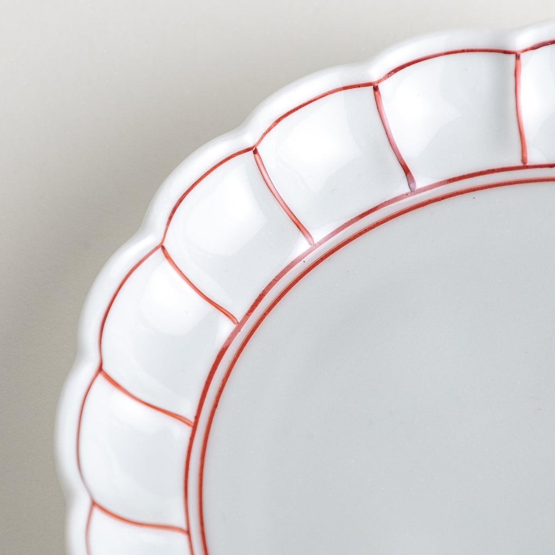 White dessert plate with scalloped edges, outlined in a thin blue or red line.