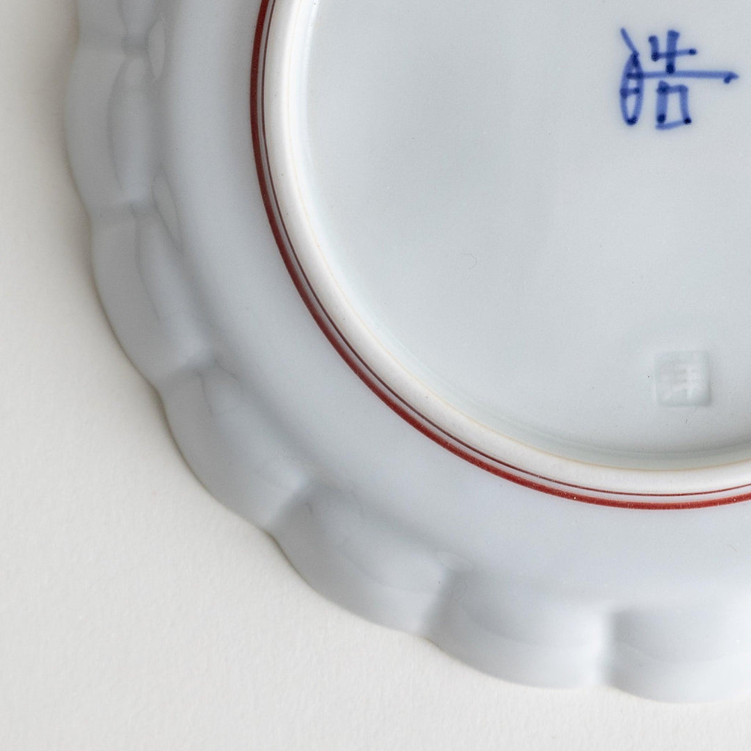 White dessert plate with scalloped edges, outlined in a thin blue or red line.