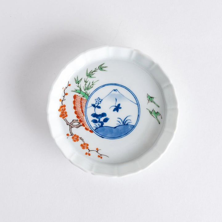 A small round plate with a traditional Japanese design depicting a landscape and floral elements.