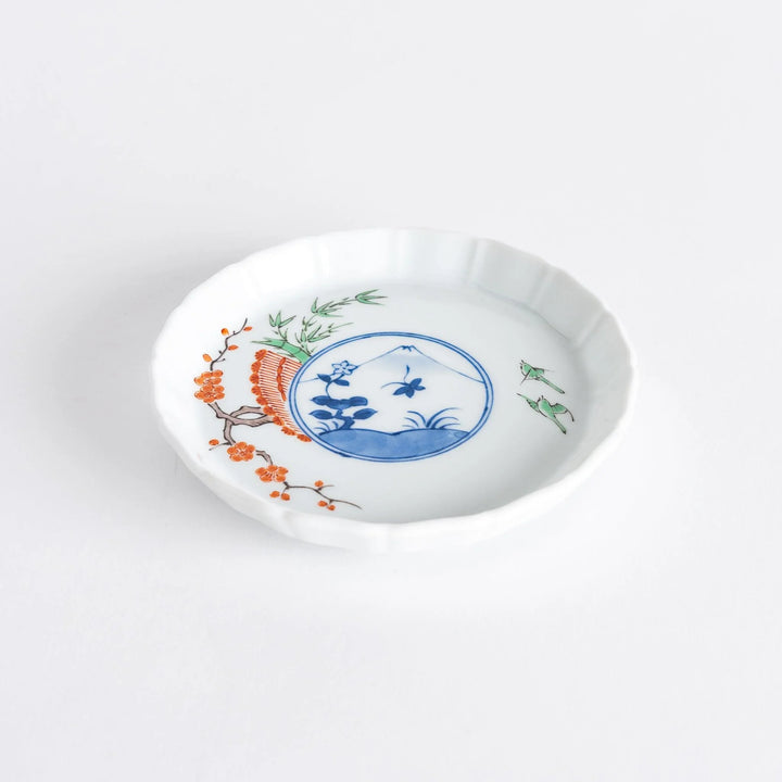 A small round plate with a traditional Japanese design depicting a landscape and floral elements.