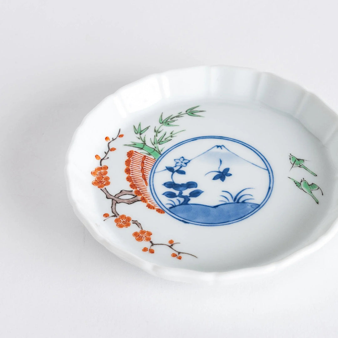A small round plate with a traditional Japanese design depicting a landscape and floral elements.