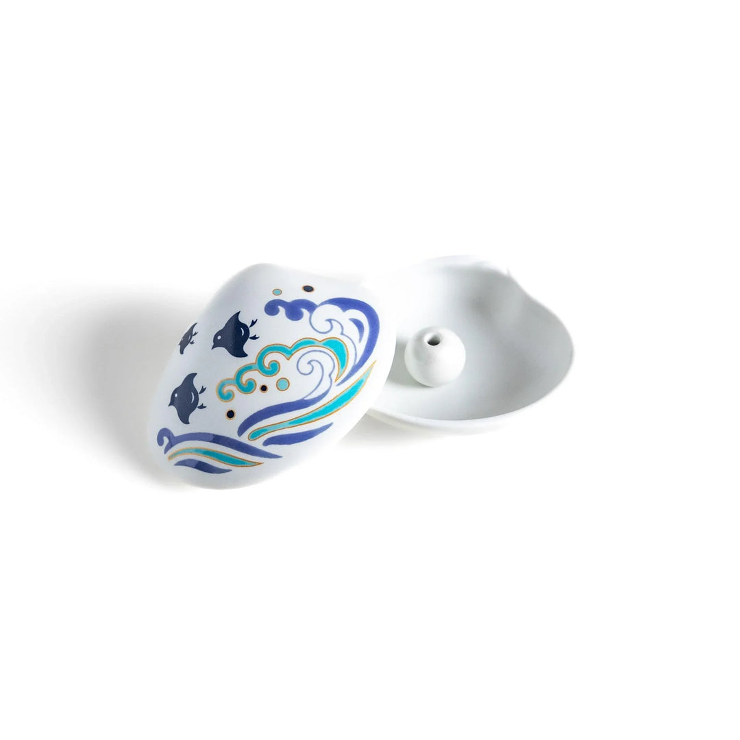 White seashell-shaped ceramic incense holder with blue wave and seabird motif and rounded holder for secure placement.