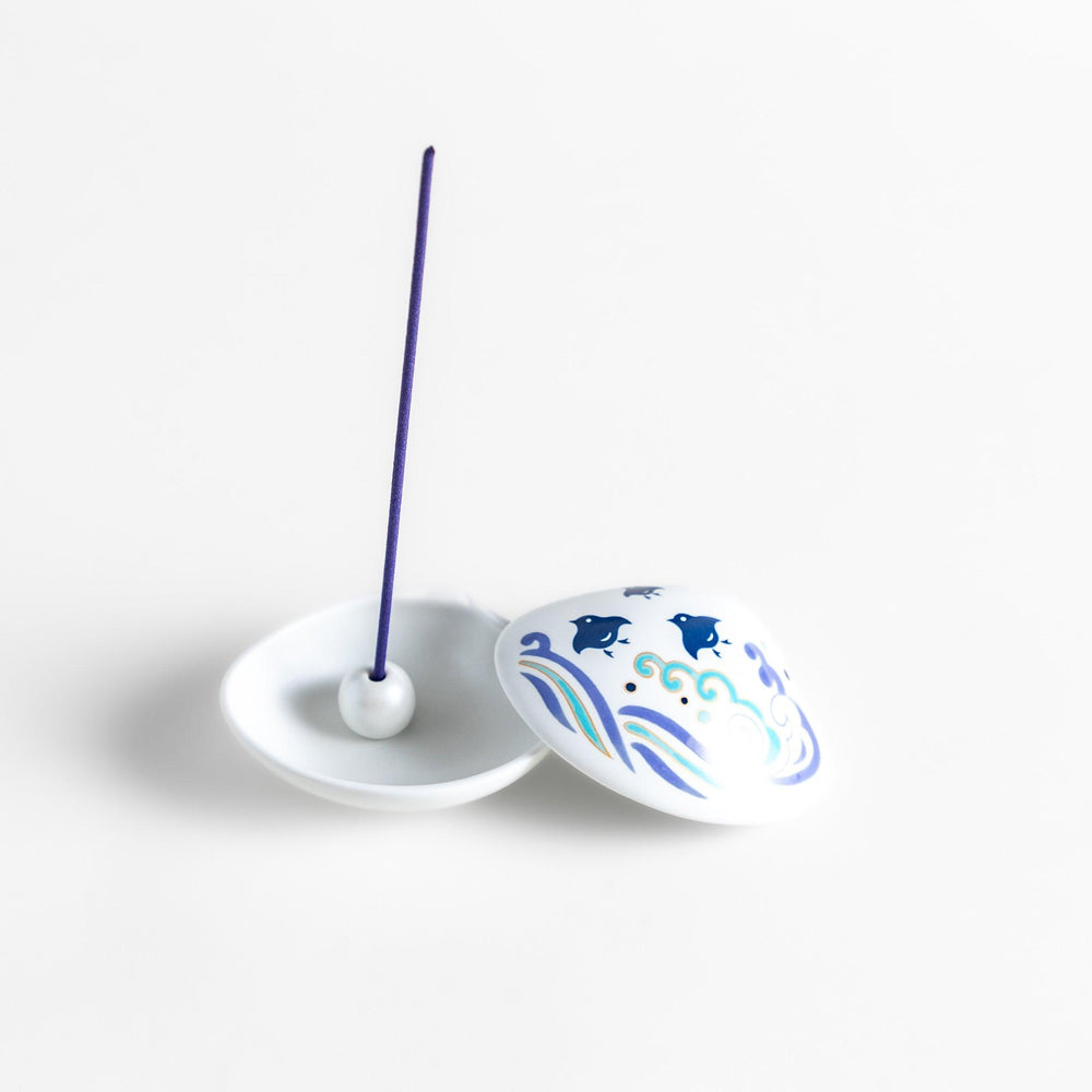 White seashell-shaped ceramic incense holder with blue wave and seabird motif and rounded holder for secure placement.